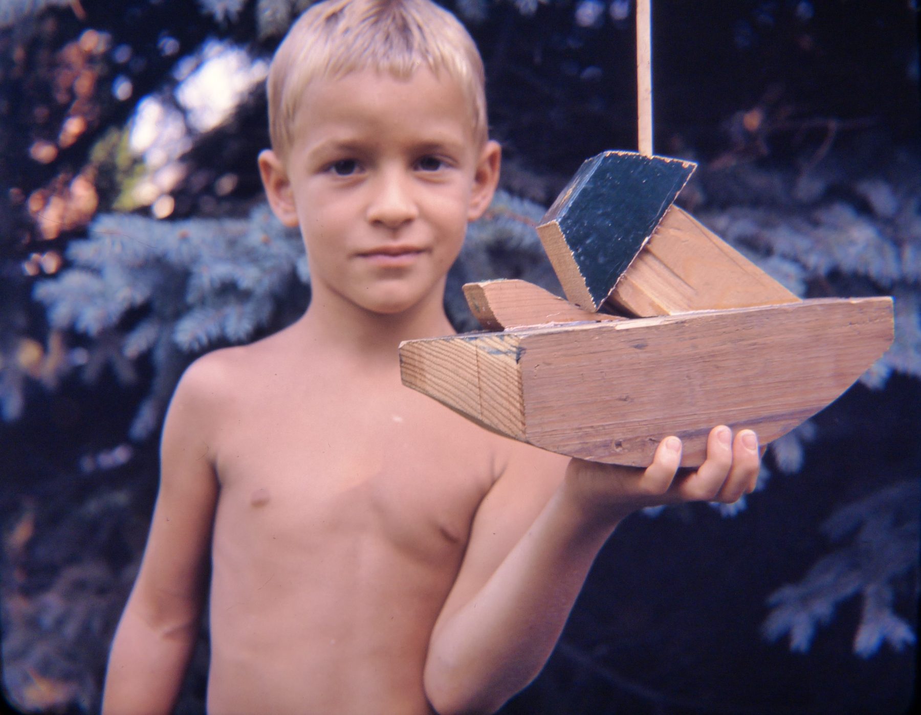 A boy holding up a handmade wooden boat
