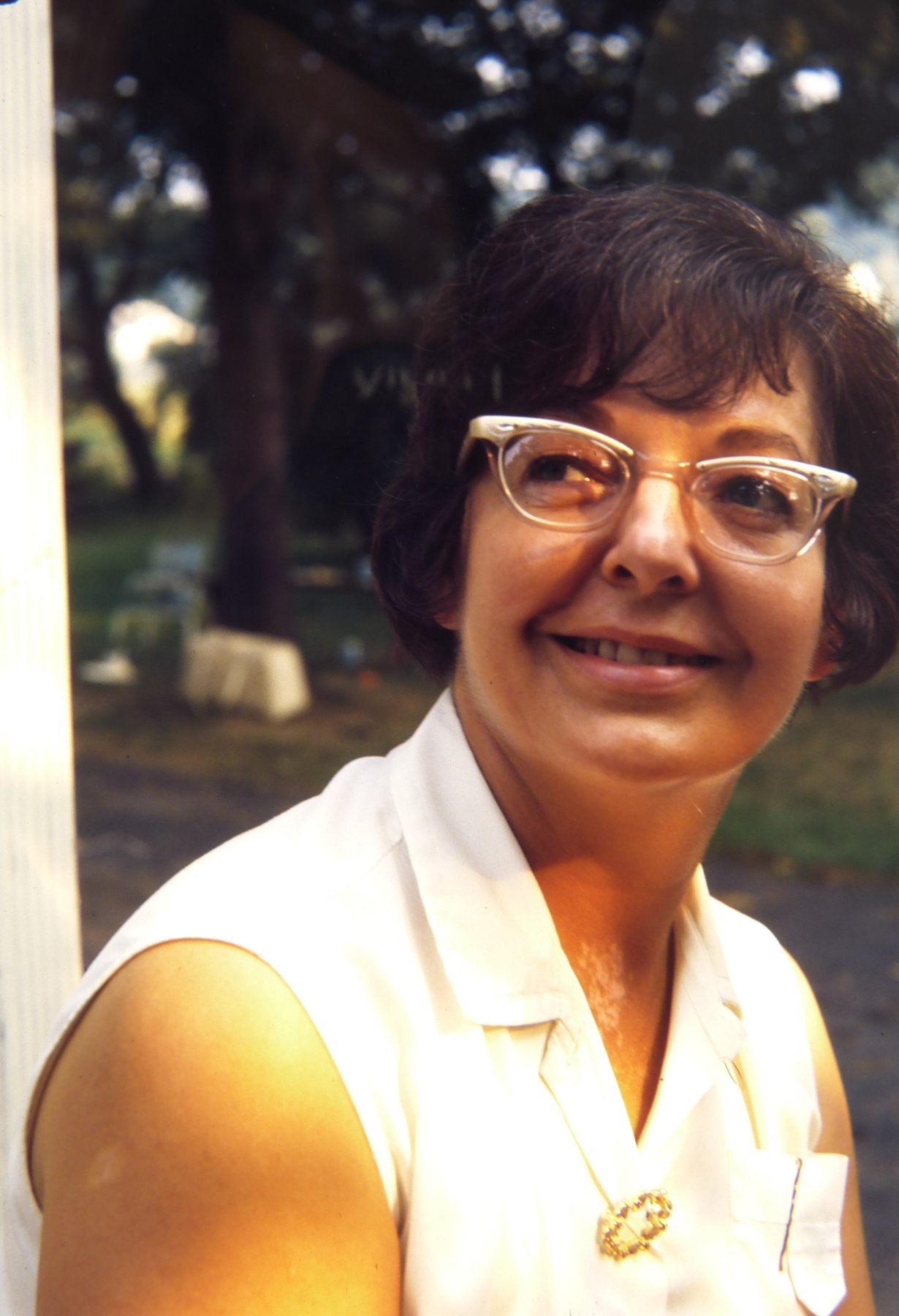 A woman in cat-eye glasses smiling on a porch