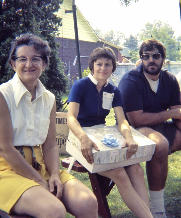 Three relatives on a bench in the yard, one holding a wrapped gift