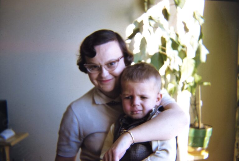 A woman hugging a small boy by a sunny window