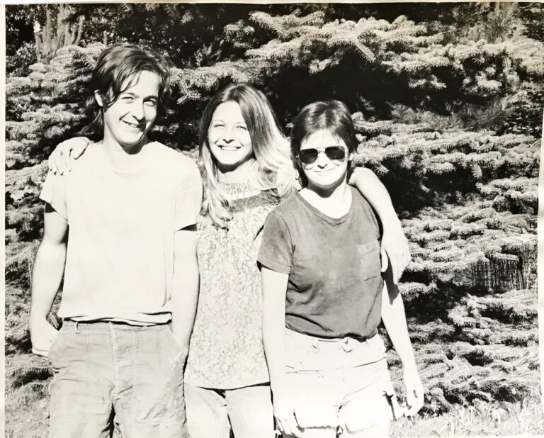 Three young relatives arm in arm in front of evergreens