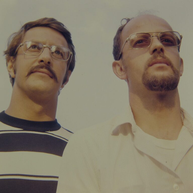 Two men in 1970s glasses looking up at the camera